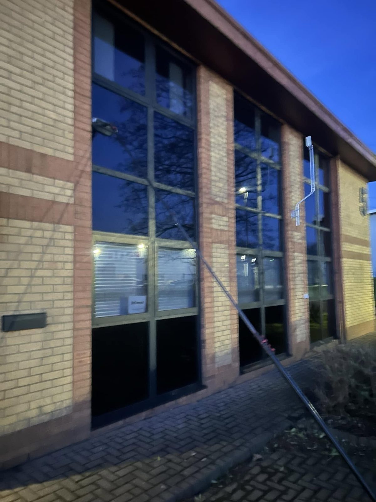 Pole cleaning a two storey glazed office frontage at dusk