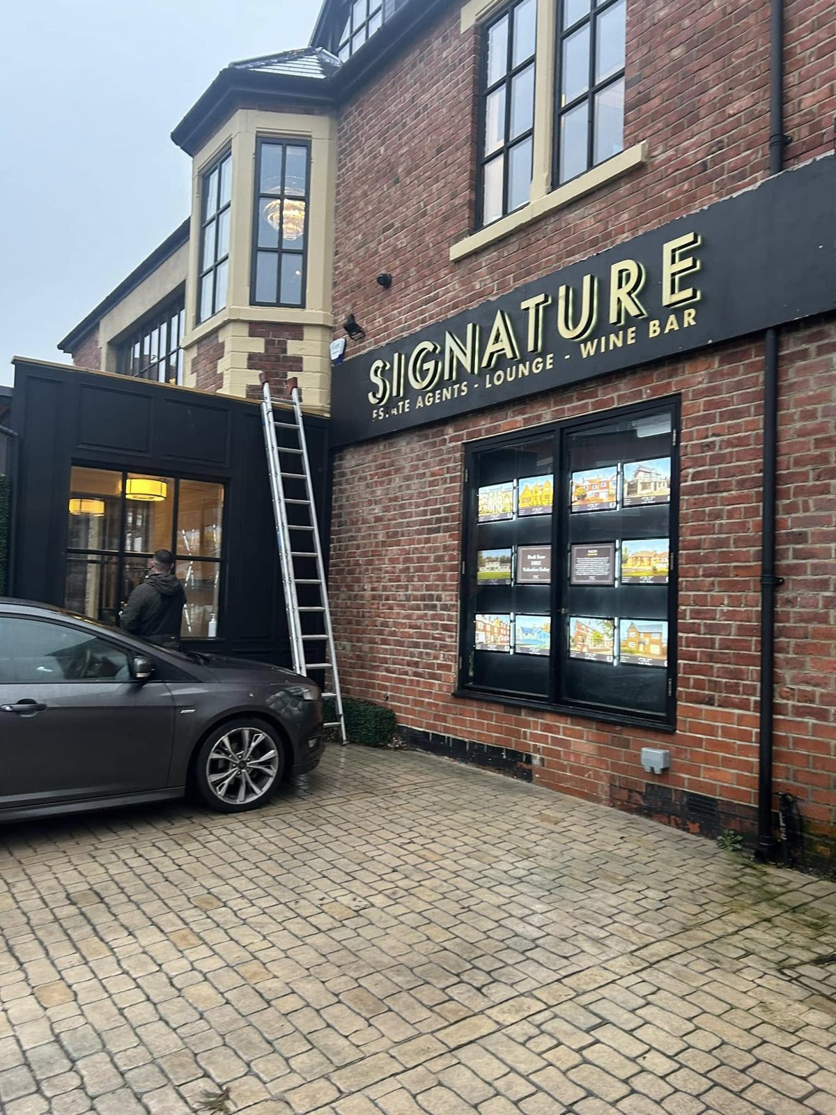 Ladder up against the front of the Signature wine bar and estate agents