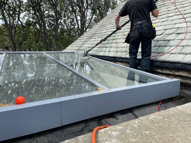 Jet washing a glass conservatory roof from the slate roof above