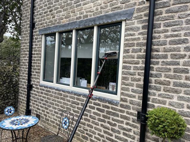 Water fed pole cleaning the windows of a stone cottage